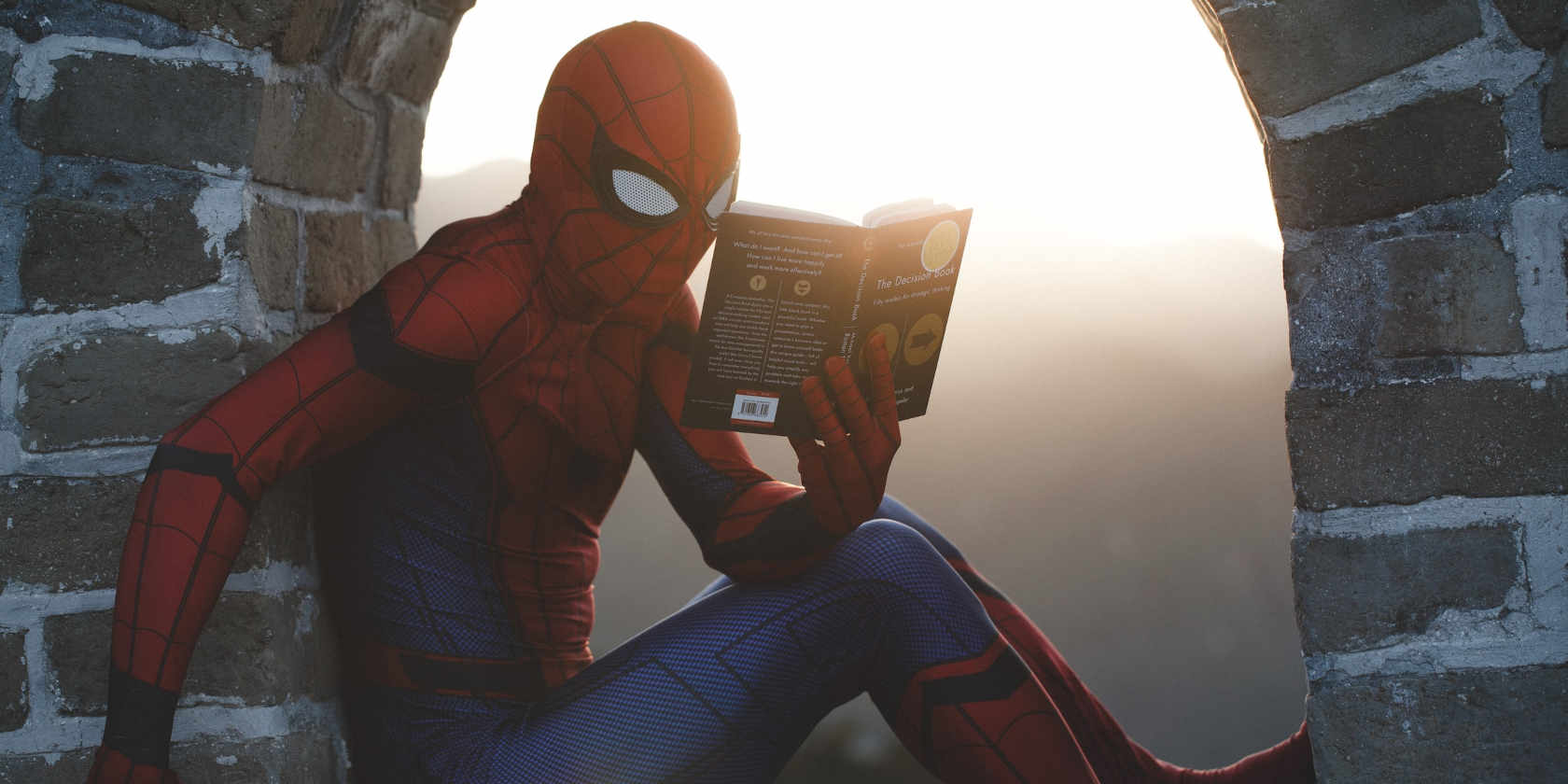 Spiderman reading a paperback, perched under a brick arch