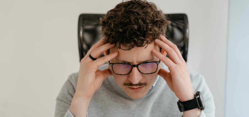 A man with glasses, clutching his head