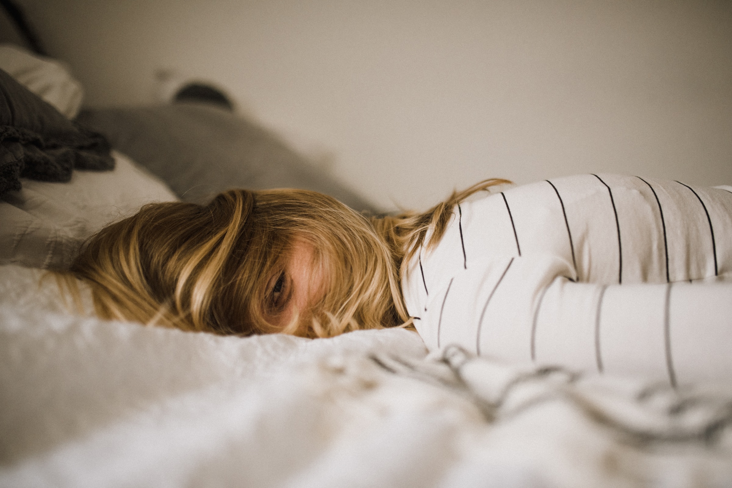 A girl lying on a bed wearing a stripy jumper. she has one eye open