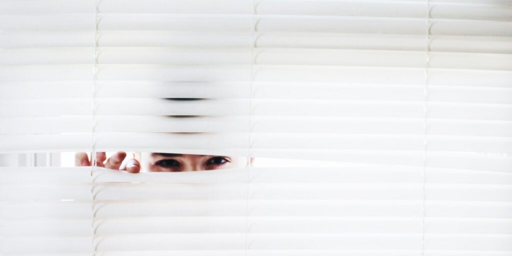 man peeking through ventian blinds through a window