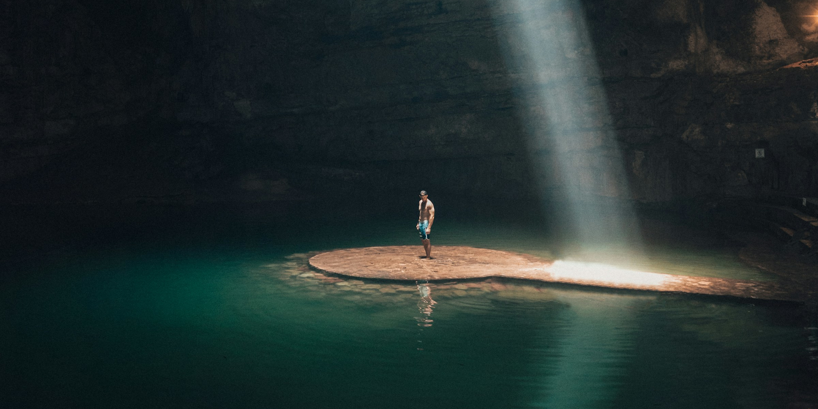 Man standing on a small island in an underground cave. A shaft of sunlight illuminates the sand behind him