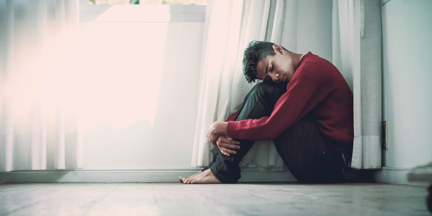 Man in a red jumper and no shoes hugging his knees