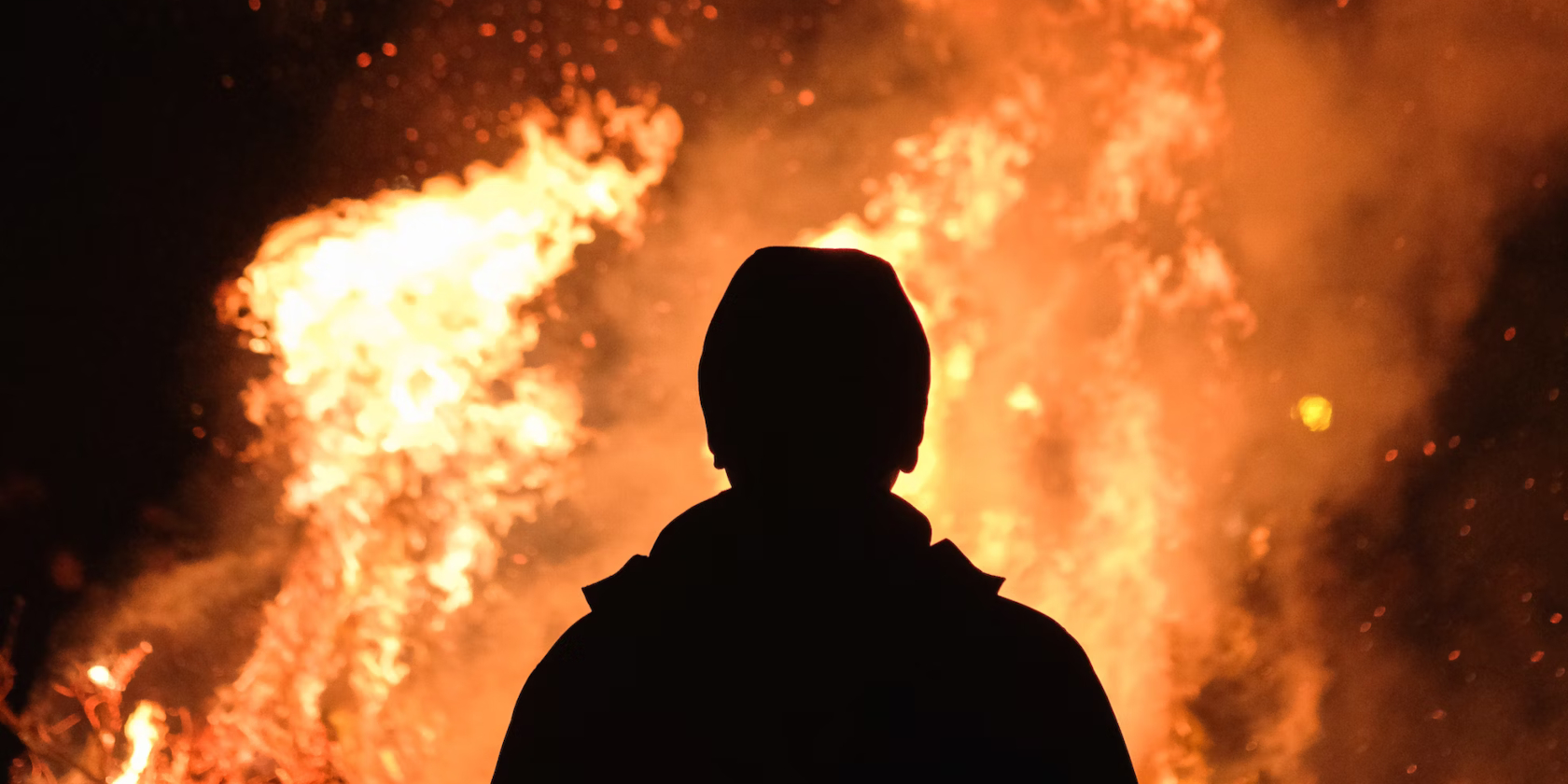 silhouette of a man in front of a blazing bonfire