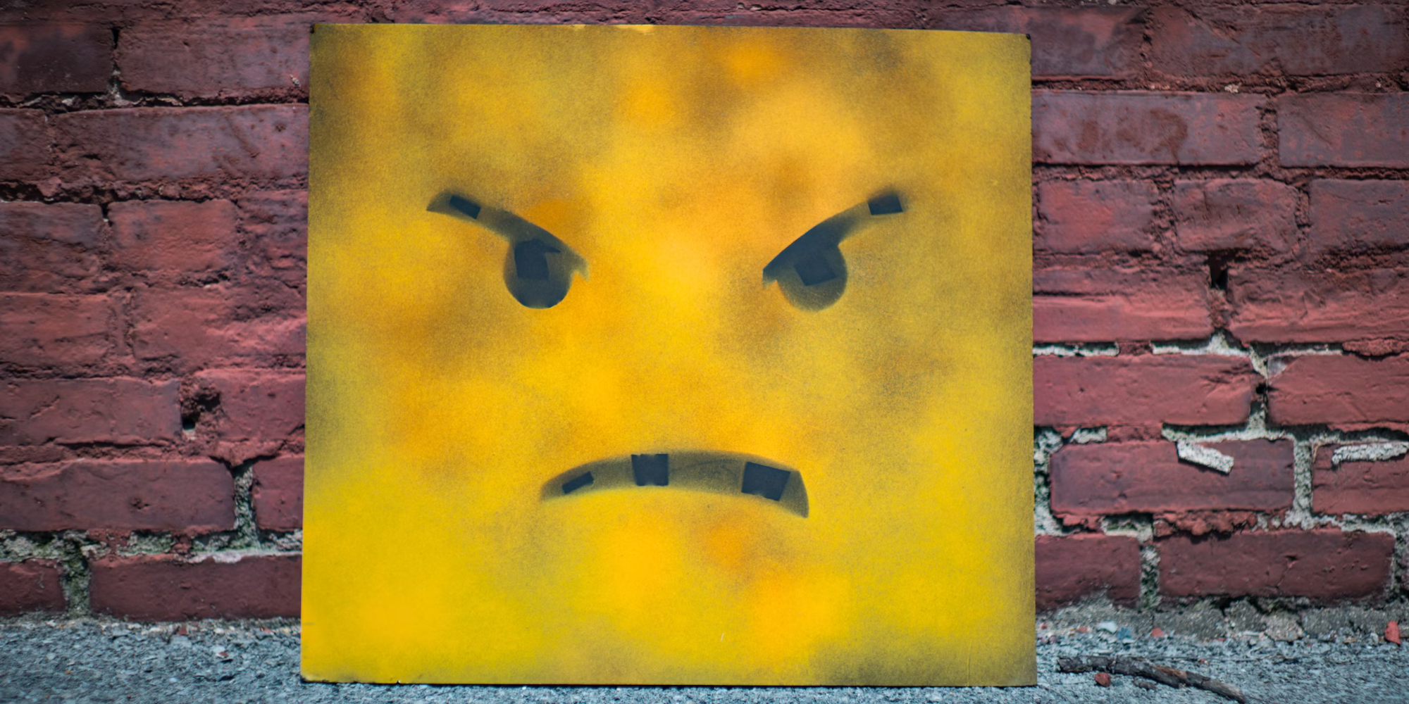 A face stencilled in black on a yellow paving slab leaning against a brick wall