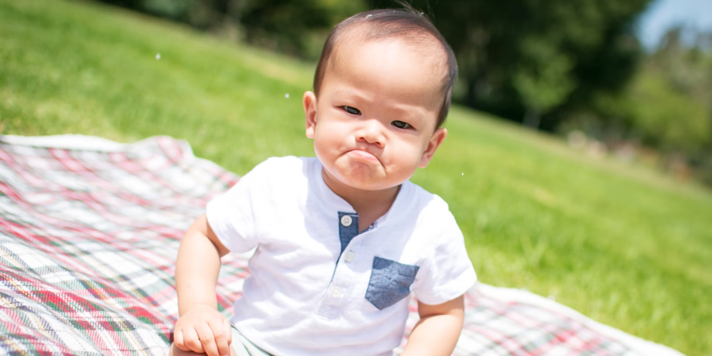 A sad baby outside on a picnic blanket