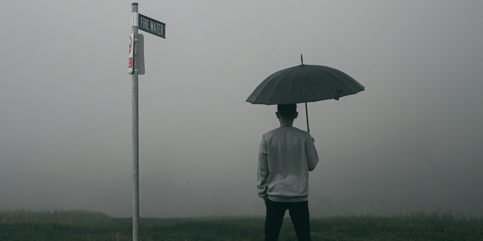 Man with umbrella standing next to a signpost near a fog bank