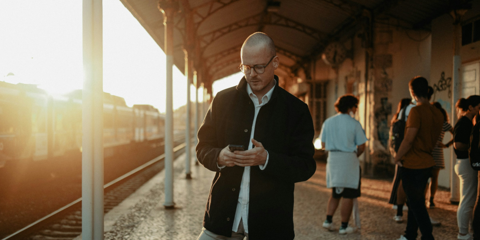 A shaven-headed man looking at his phone in a train station