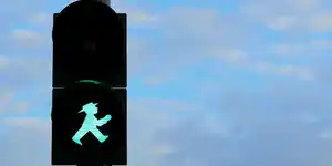 Traffic signal showing a green man in a hat walking. There is a blue sky in the background