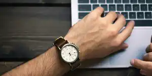 A man's arm and wristwatch resting on a laptop keyboard